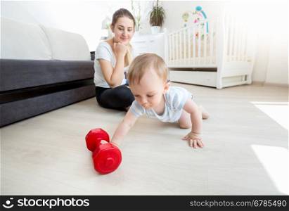 Young beautiful mother with her baby boy exercising with dumbbells on floor at living room
