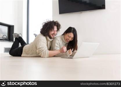 Young beautiful multiethnic couple using a laptop and doing shopping online at home on the floor