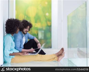 Young beautiful multiethnic couple using a laptop and doing shopping online while sitting on the floor