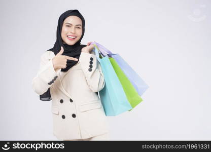 Young beautiful muslim woman in suit holding colorful shopping bags over white background studio