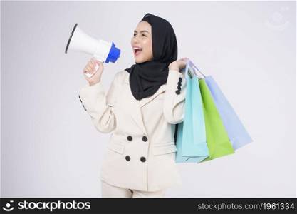 Young beautiful muslim woman in suit holding colorful shopping bags over white background studio