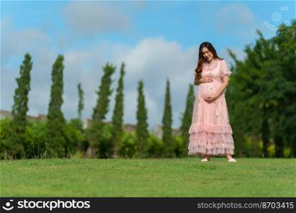 young beautiful pregnant woman looking and stroking her belly in the park