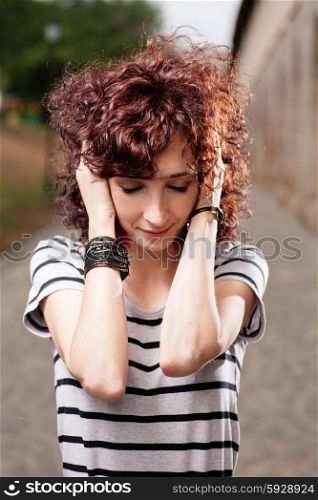 Young beautiful red curly hair woman at the park looking down and holding her head by hands