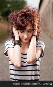 Young beautiful red curly hair woman at the park looking down and holding her head by hands