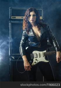 Young beautiful redhead woman playing an electric guitar in front of large amplifier.