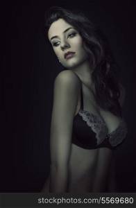 young beautiful sexy girl wearing a fashion bra , and posing on dark background. she has hairstyle looking down