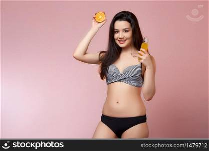 young beautiful slender Asian girl in a swimsuit . with fresh juice and an orange in his hands. smiles. on a pink isolated background.