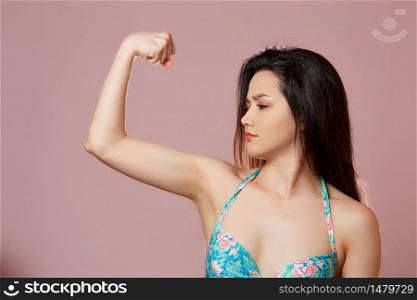young beautiful slender Asian girl in a swimsuit shows her arm, biceps . on a pink isolated background