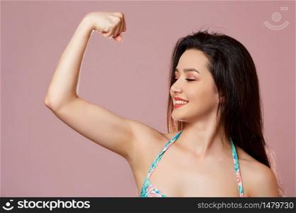 young beautiful slender Asian girl in a swimsuit shows her arm, biceps . on a pink isolated background