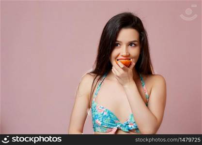 young beautiful slender Asian girl in a swimsuit . with apple in his hands. smiles. on a pink isolated background.