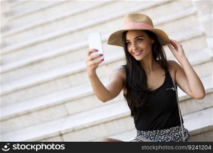 Young beautiful smiling woman in hat making selfie with smartphone outdoors