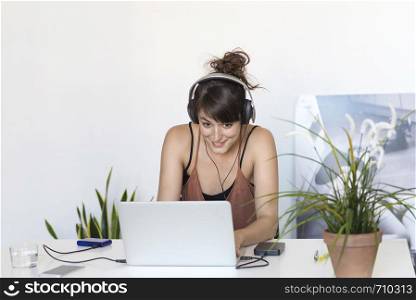 Young beautiful smiling woman with headphones sitting working with laptop on table.. Rafa Fernandez