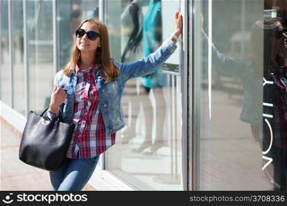 Young beautiful stylish girl in sunglasses and with a bag in hand on a sunny day on the streets of major cities.