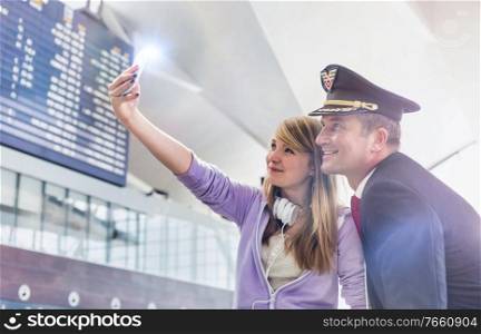 Young beautiful teenage girl taking selfie with mature pilot in airport