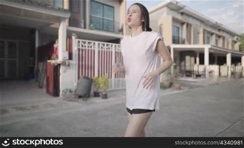 young beautiful white asian in casual outfits running on village street, female runner jogging and blowing mouth, follow view of athlete woman training jogging on to sunlight, healthy lifestyle