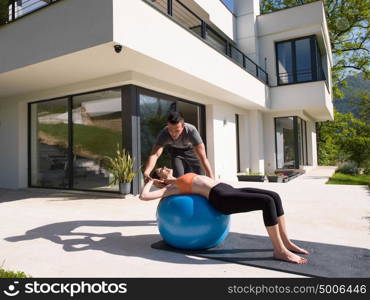 young beautiful woman and personal trainer doing exercise with pilates ball in front of her luxury home