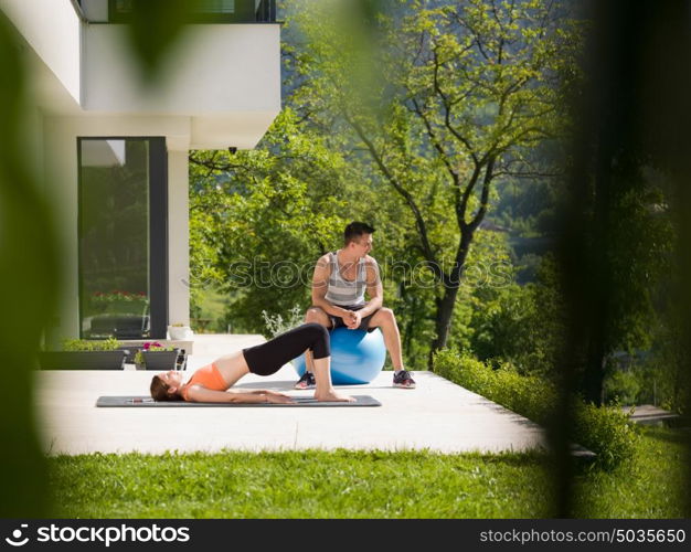 young beautiful woman and personal trainer doing exercise with pilates ball in front of her luxury home