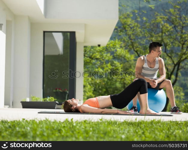 young beautiful woman and personal trainer doing exercise with pilates ball in front of her luxury home