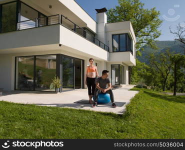 young beautiful woman and personal trainer doing exercise with pilates ball in front of her luxury home