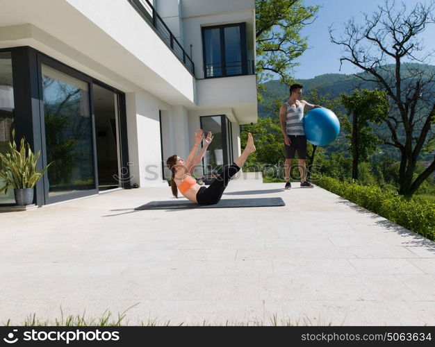 young beautiful woman and personal trainer doing exercise with pilates ball in front of her luxury home