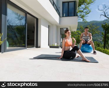 young beautiful woman and personal trainer doing exercise with pilates ball in front of her luxury home