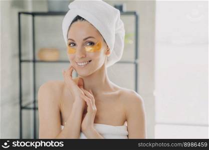 Young beautiful woman applies anti wrinkle eye patches. Attractive caucasian woman wrapped in towel after spa procedures. Happy girl does hair and body care. Relaxation at modern spa resort.. Young beautiful woman applies anti wrinkle eye patches. Happy girl does hair and body care.