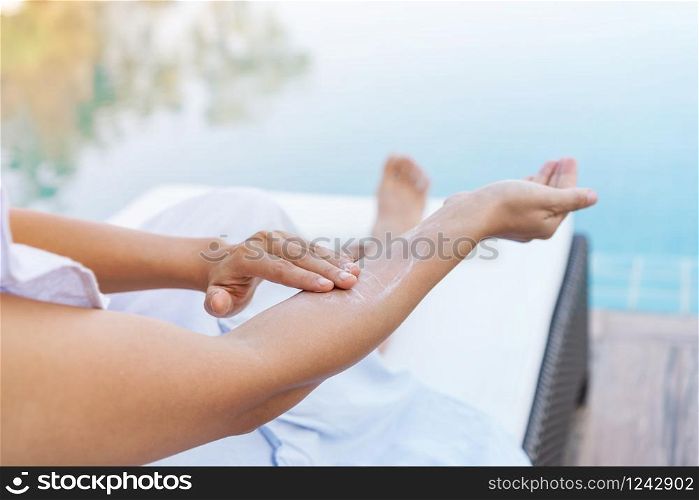Young beautiful woman applying sunscreen or suntan lotion in her body for solar skin protection at swimming pool. Brunette girl enjoying summer vacation.