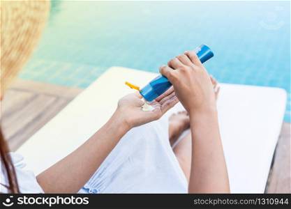 Young beautiful woman applying sunscreen or suntan lotion in her body for solar skin protection at swimming pool, summer holidays concept.