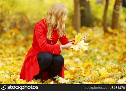 Young beautiful woman collecting autumnal leaves in park
