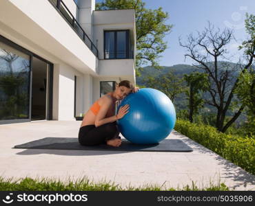 young beautiful woman doing exercise with pilates ball in front of her luxury home villa