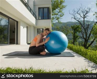 young beautiful woman doing exercise with pilates ball in front of her luxury home villa