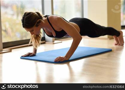 Young beautiful woman doing pushups in the gym on blue mat. Girl wearing sportwears clothes.