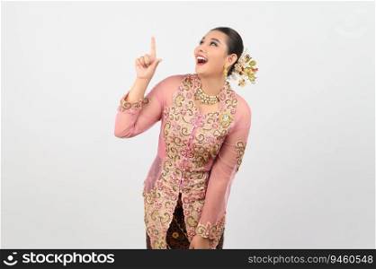 Young beautiful woman dress up in local culture in southern region with charming gesture smile, looking and point finger up on white background, copy space