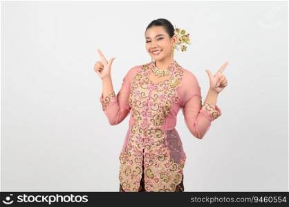 Young beautiful woman dress up in local culture in southern region with charming gesture smile and two hands point finger on white background, copy space