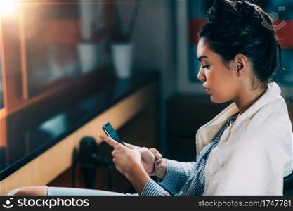Young beautiful woman getting revitalizing hair treatment in beauty salon. Sitting and using her smart phone.. Young beautiful woman using her smart phone in beauty salon