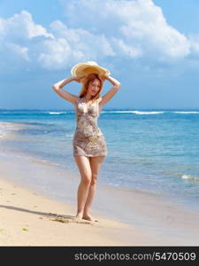 Young beautiful woman goes on ocean coast with straw hat in hands