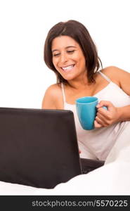 Young beautiful woman having breakfast in bed while working or relaxing with her computer