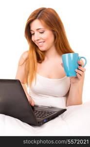 Young beautiful woman having breakfast in bed while working or relaxing with her computer