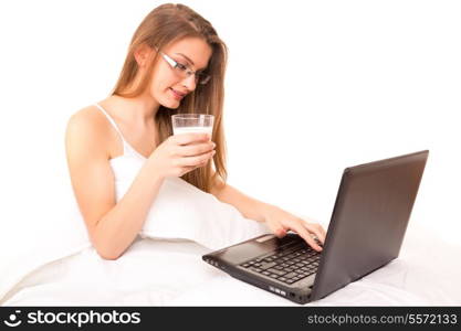 Young beautiful woman having breakfast in bed while working or relaxing with her computer