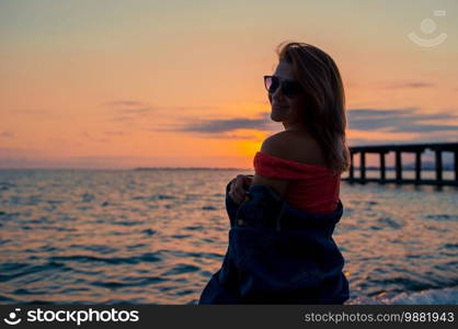 Young beautiful woman having fun on tropical seashore at sunset. Outdoor fashion portrait of stylish girl wearing trendy sunglasses and jeans jacket on the beach.