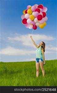 Young beautiful woman having fun with balloons on a green meadow