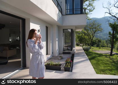 young beautiful woman in a bathrobe enjoying morning coffee in front of her luxury home villa