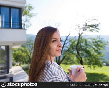 young beautiful woman in a bathrobe enjoying morning coffee in front of her luxury home villa