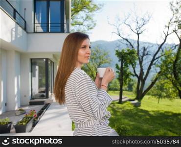 young beautiful woman in a bathrobe enjoying morning coffee in front of her luxury home villa