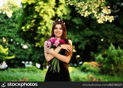 Young beautiful woman in a black dress posing with a bouquet of peonies in a garden. Fashion model girl with bunch of flowers outdoors in summer