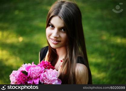 Young beautiful woman in a black dress posing with a bouquet of peonies in a garden. Fashion model girl with bunch of flowers outdoors in summer