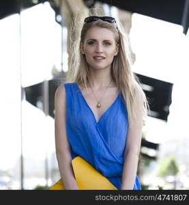 Young beautiful woman in a blue dress and a yellow bag on the background of shop windows