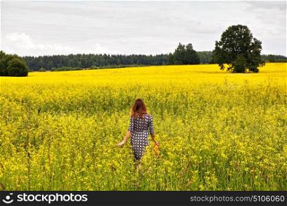 Young beautiful woman in a flowering rapeseed field walking back to the camera. Blooming colza field. Summer concept. agriculture concept.