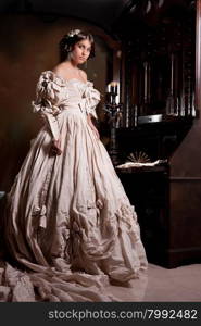 Young beautiful woman in a wedding dress standing near the old secretaire