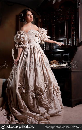 Young beautiful woman in a wedding dress standing near the old secretaire